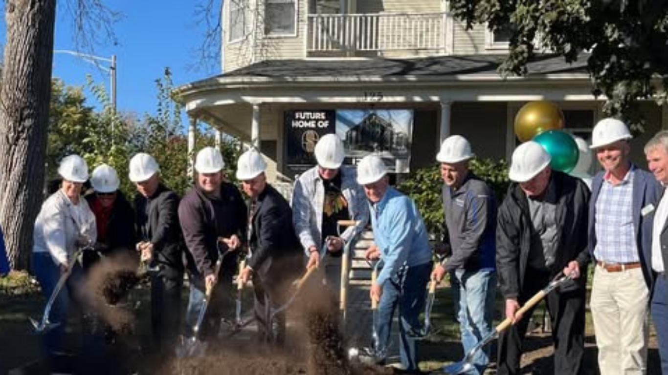 A group of people wearing hardhats and holding shovels stand in front of a building